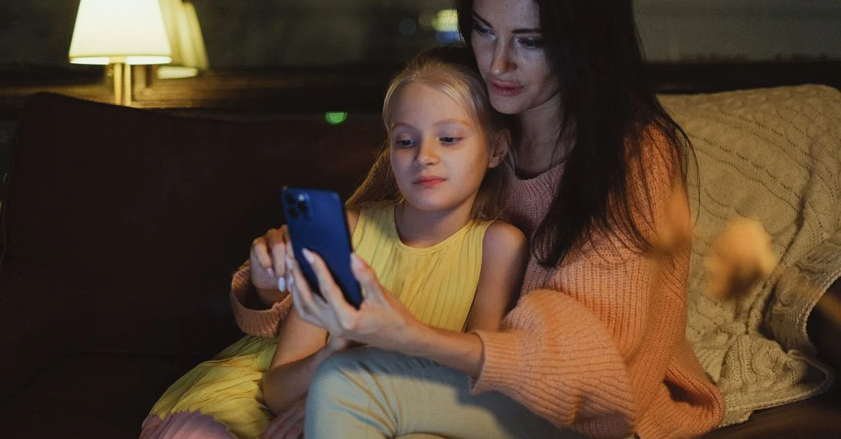 Une mère et sa fille passent un bon moment ensemble sur un canapé confortable, regardant un smartphone.