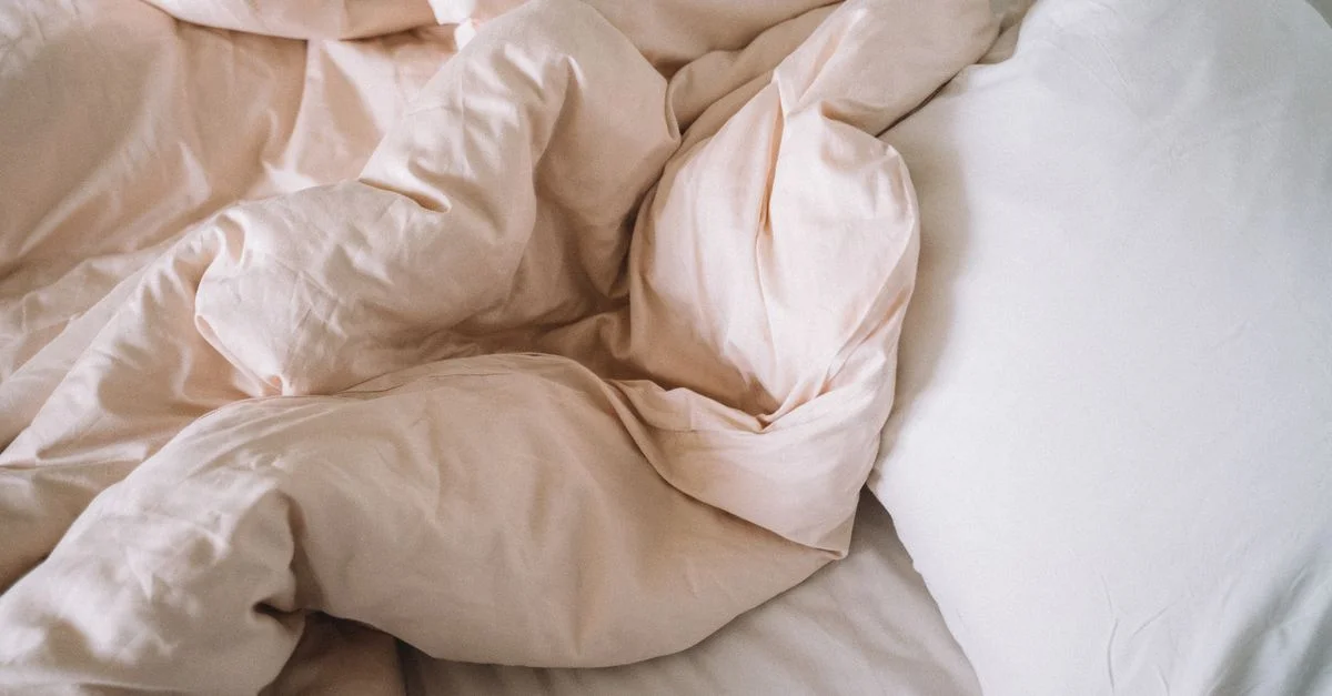 Des draps de lit doux et froissés avec un coussin évoquent un sentiment de confort et de relaxation dans une chambre.
