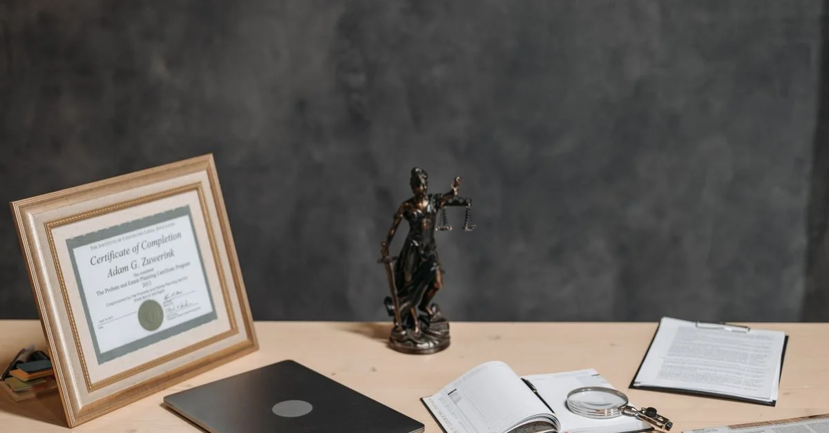 Un bureau d'avocat avec une statue de la justice, un diplôme, un ordinateur portable, une loupe et des documents.