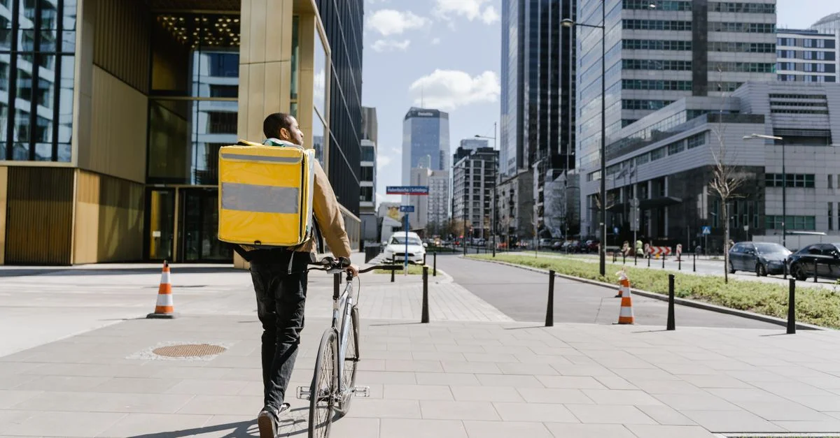 Livreur à vélo circulant dans une rue de la ville avec un sac de livraison, thème de logistique urbaine.