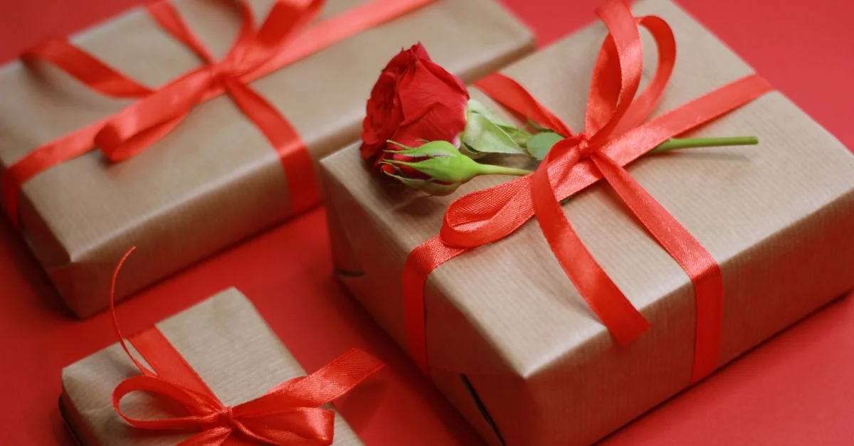 Coffrets cadeaux élégants noués avec des rubans rouges et une rose sur fond rouge.